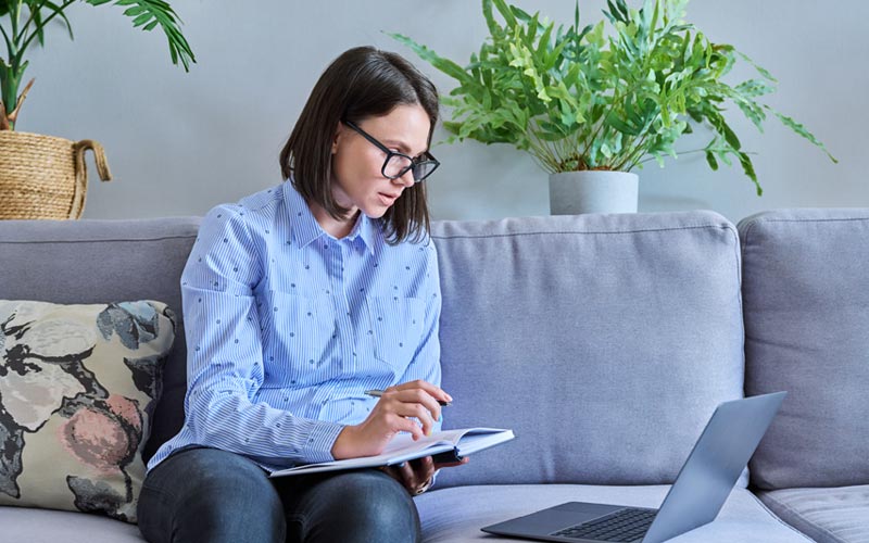 A female first time business owner sitting on a sofa with a laptop considering buying a franchise